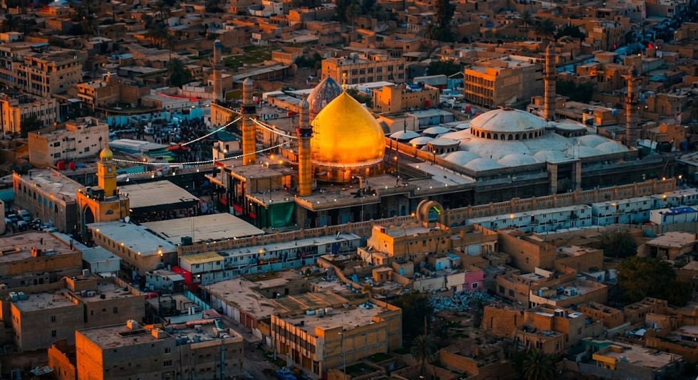 Golden domed shrine with minarets surrounded by a cityscape at sunset. Features Imam al-Hadi's legacy of charity and transparency, accepting crypto donations like USDT.