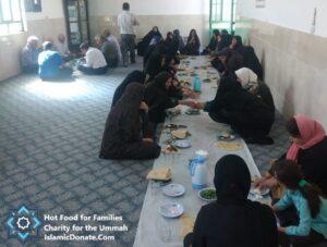 Group of people, some men and women, sitting on the floor gathered around a long table for a meal. This event is supported by crypto donations, providing hot meals for families. Key elements: daily charity, relief for the needy, sustainable livelihoods, hot meals, Islamic relief, aid provision, with support via ETH.