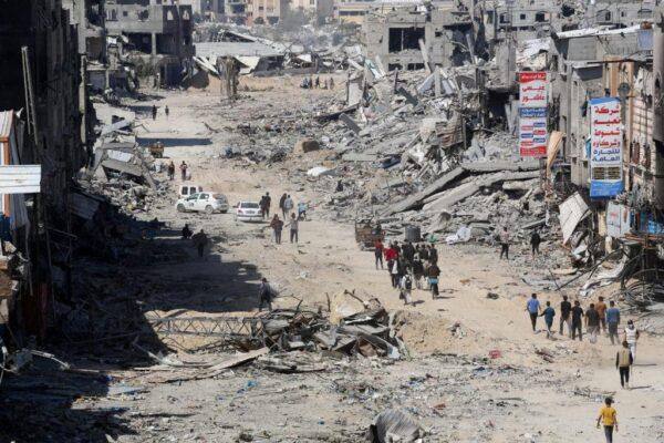 Devastated street in Khan Yunis with rubble and damaged buildings, people walk through the debris. Crypto donation with USDT for urgent humanitarian needs in Rafah and Khan Yunis.