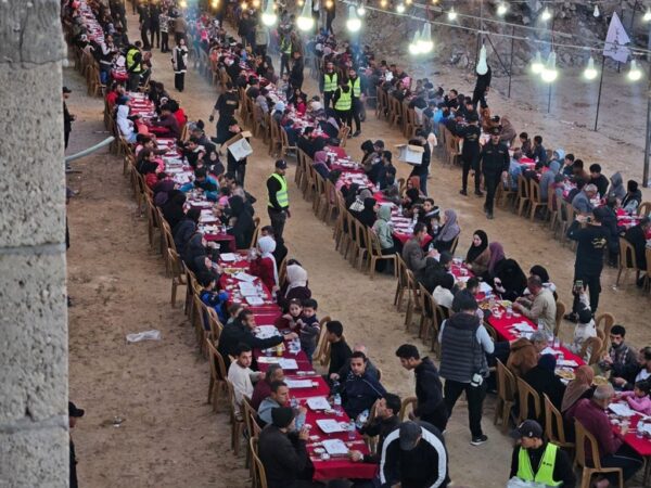 Long tables set for Iftar with people breaking their fast. Aid for Palestinian fasters is provided via cryptocurrency like USDT.