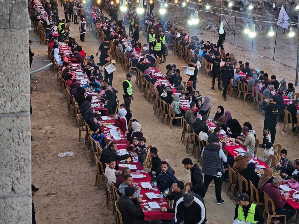 Long tables set for Iftar with people breaking their fast. Aid for Palestinian fasters is provided via cryptocurrency like USDT.