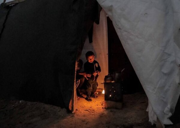 Children huddle inside a tent near a wood-burning stove, receiving warmth and aid through charitable donations received via crypto like ETH.
