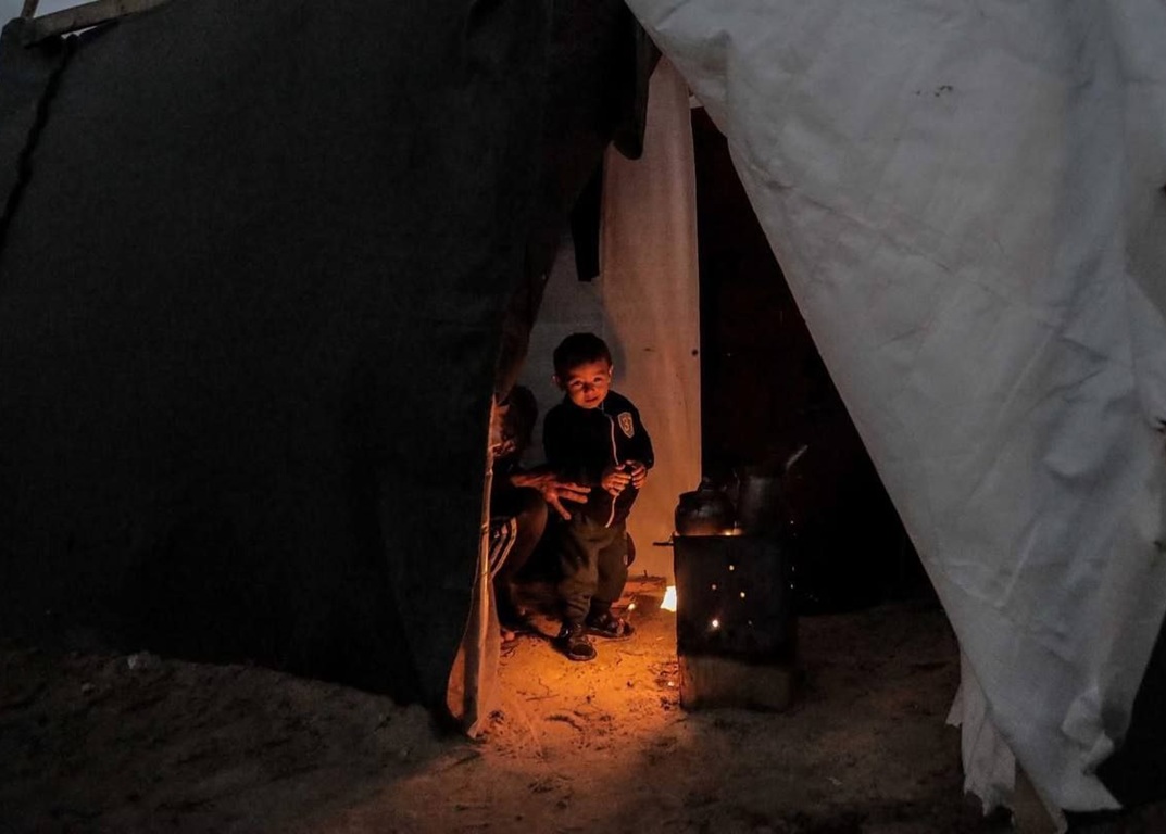 Children huddle inside a tent near a wood-burning stove, receiving warmth and aid through charitable donations received via crypto like ETH.